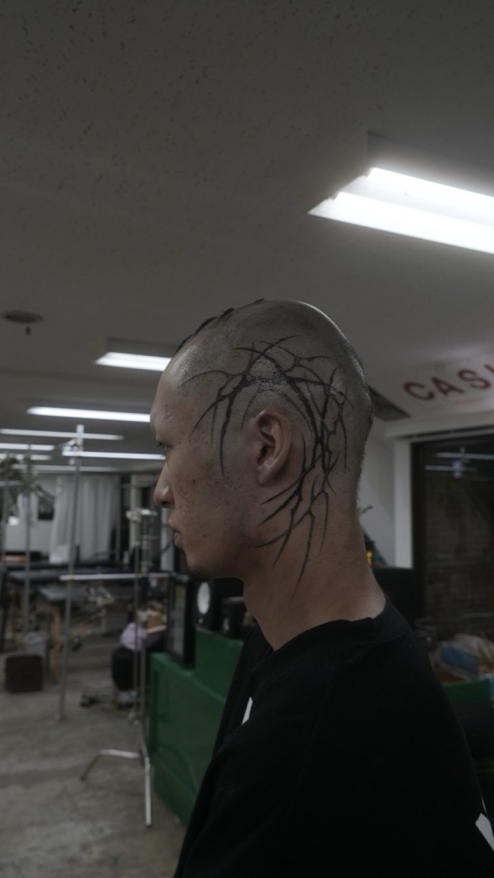 Fine black line work across a shaved head, seen in profile